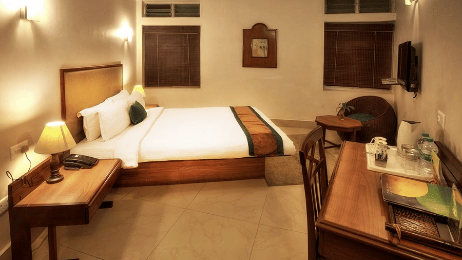 Polo Resort Cherrapunji guest room with king bed, wall sconces, bamboo blinds, wicker chair, writing desk, tea tray and tiled floor.