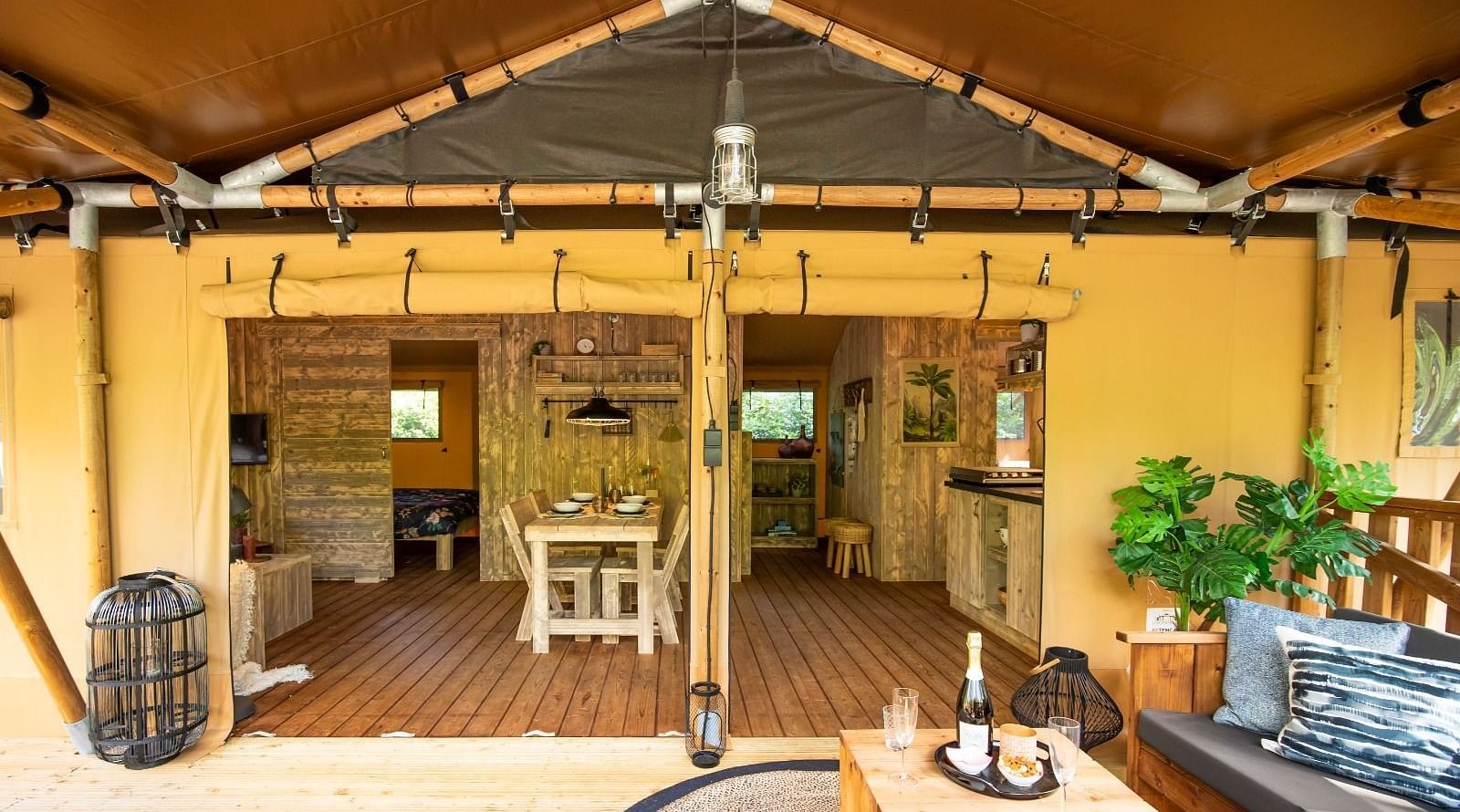A glimpse inside a tent reveals a cozy interior with wooden flooring, and a small dining table. The tent features a canvas roof and walls, suggesting a comfortable glamping experience
