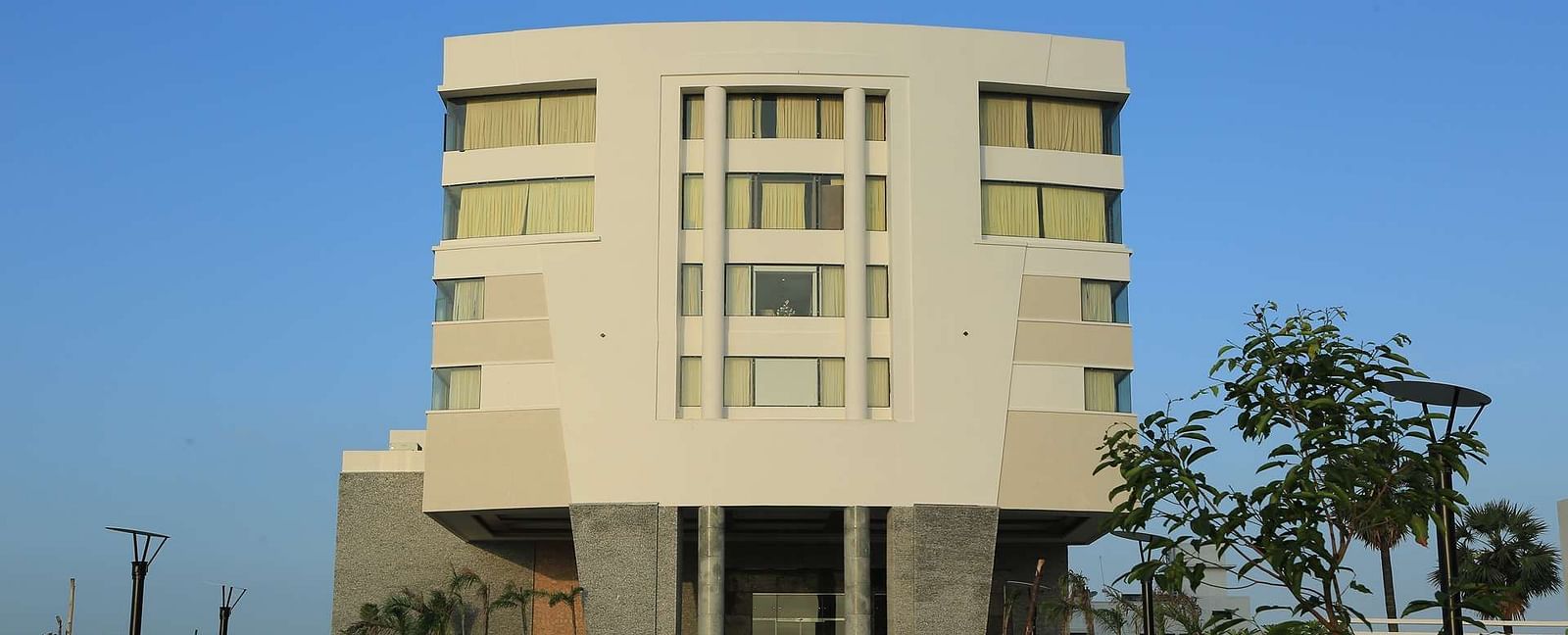 Front view of facade of Dhanalaksmi Srinivasan Hotels, Perambanur  with a backdrop of clear blue sky.