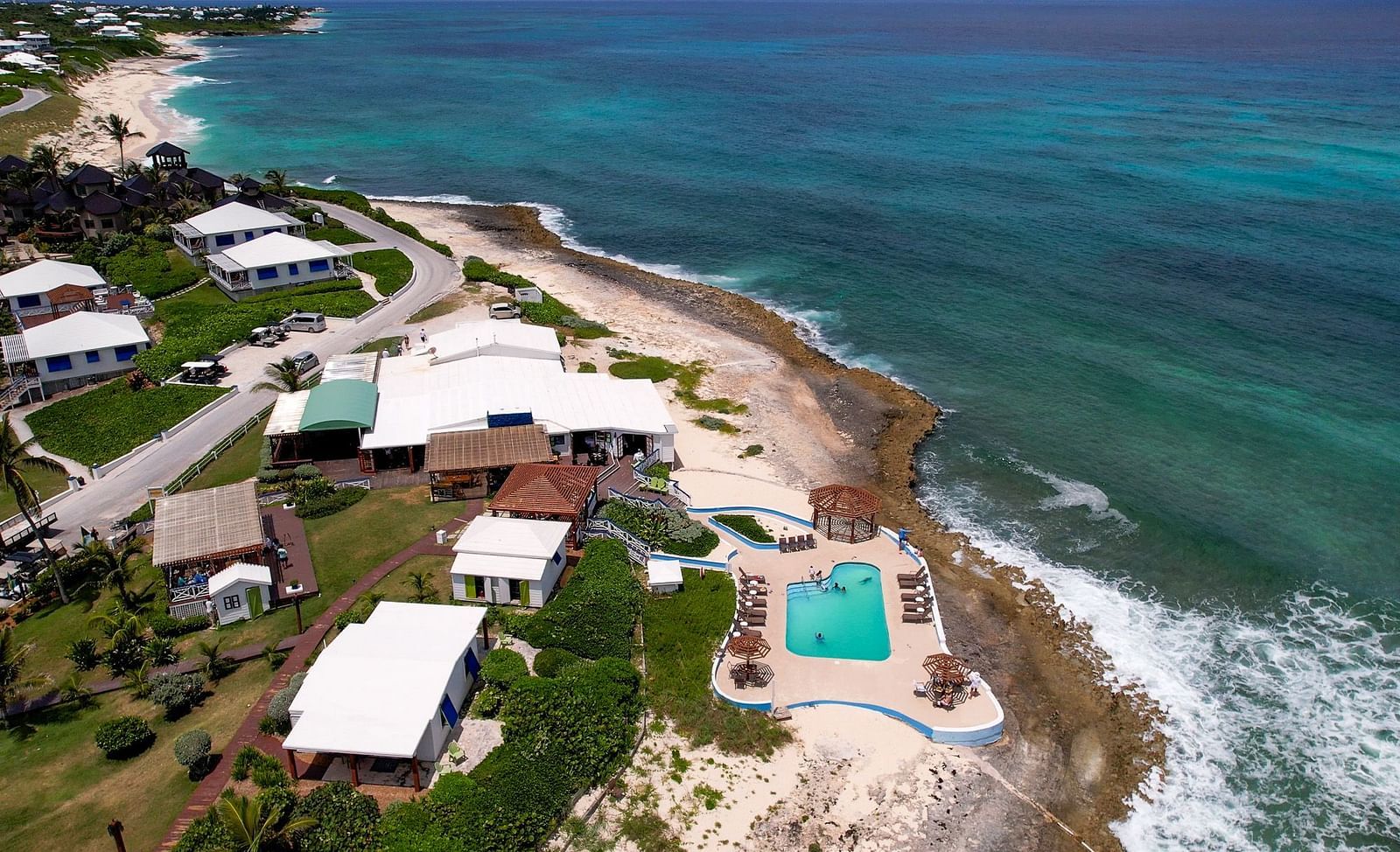 Coastal resort captured from above, featuring a swimming pool, beachside villas, and turquoise ocean waves | Abaco Inn