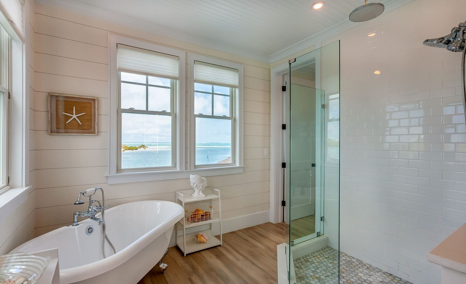 a bathroom with a bathtub, wooden floor, walk in shower, and windows that overlooks the sea at Abaco Inn.