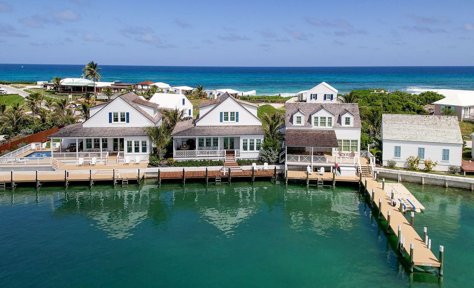 A view of coastal houses of Abaco Inn situated along a body of water with docks, facing an expansive ocean under a clear sky - Abaco Inn