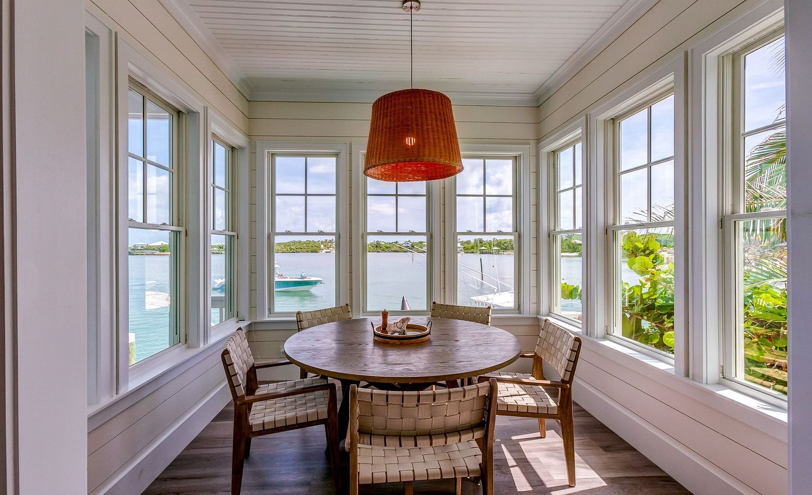 Dining nook with a round wooden table, wicker chairs, and large windows overlooking greenery | Abaco Inn