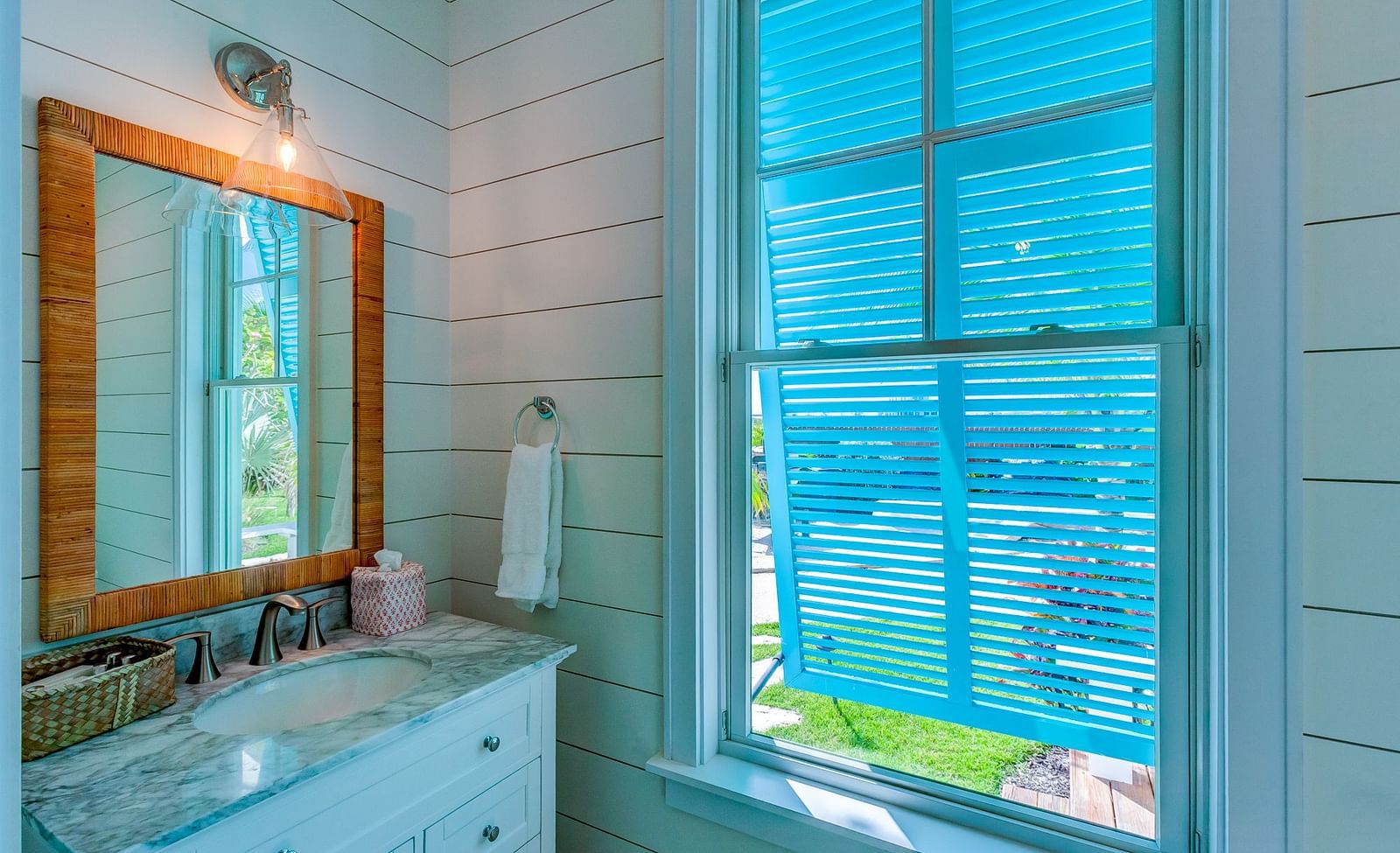 Bathroom with white vanity, wooden mirror frame, and window with blue shutters | Abaco Inn