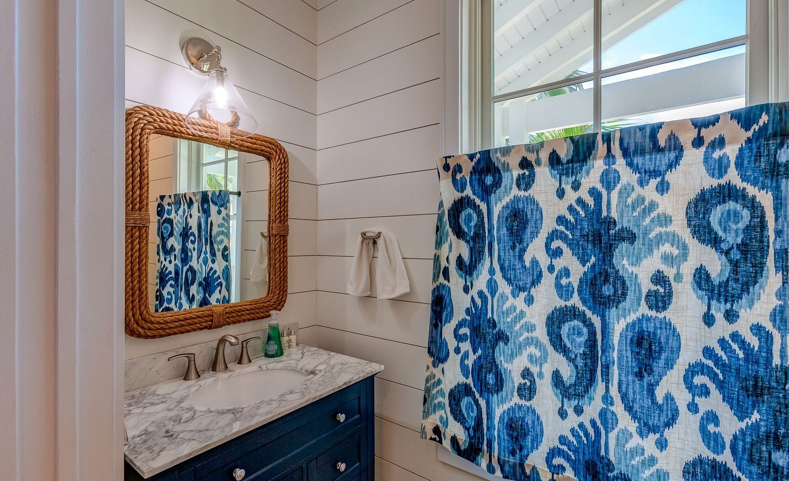 Bathroom with a white vanity, a mirror with a wooden frame, and blue paisley shower curtain | Abaco Inn