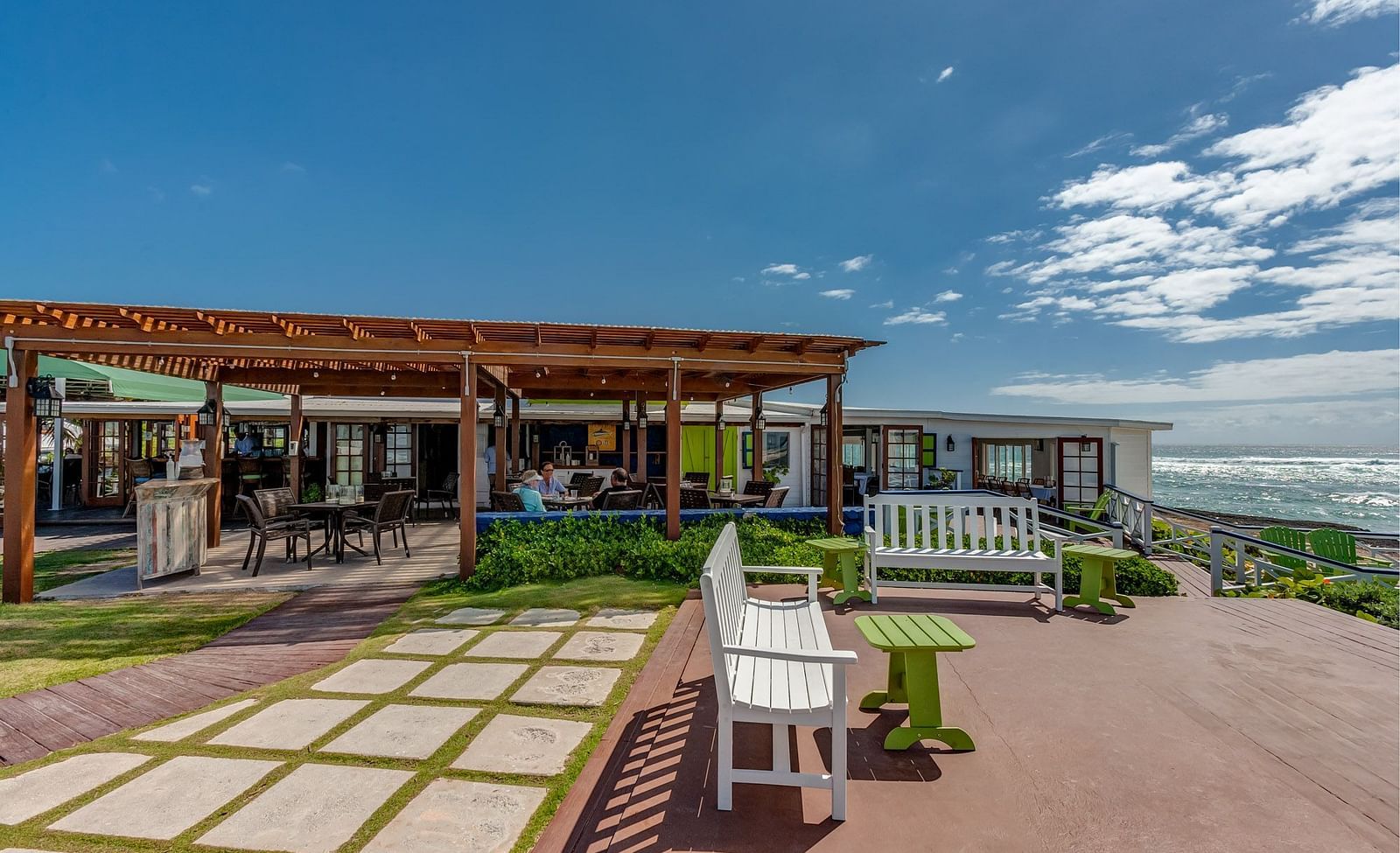 A spacious patio with a restaurant, outdoor seating, and ocean views under a partly cloudy sky.