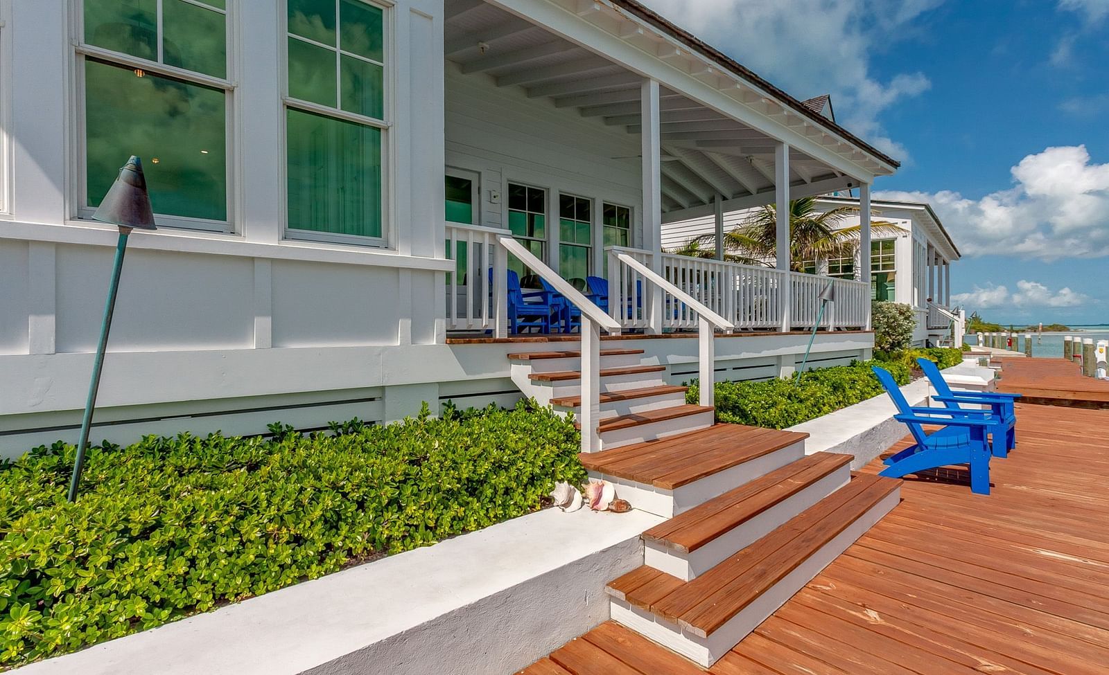 Waterfront deck with blue Adirondack chairs and a view of the calm sea | Abaco Inn