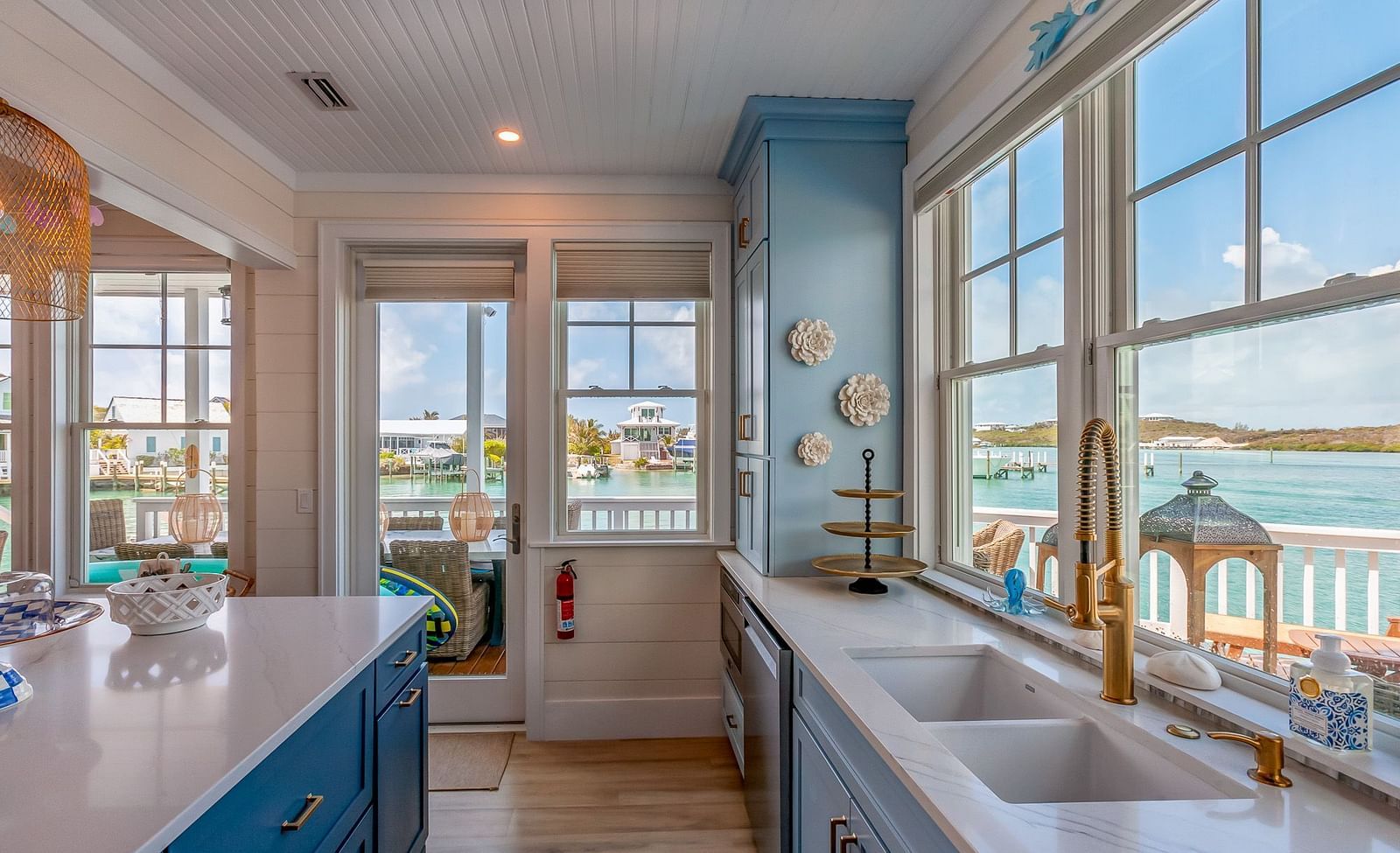 Bright, airy , white and blue coloured theme kitchen with golden taps and windows that overlooks the sea at Abaco Inn.
