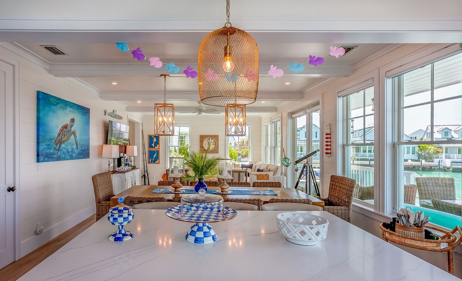 A sitting area with sofas and TV, A wooden dining table with wooden chairs, a marble top table with cupcake stands on it  and windows that overlook the sea at Abaco Inn.