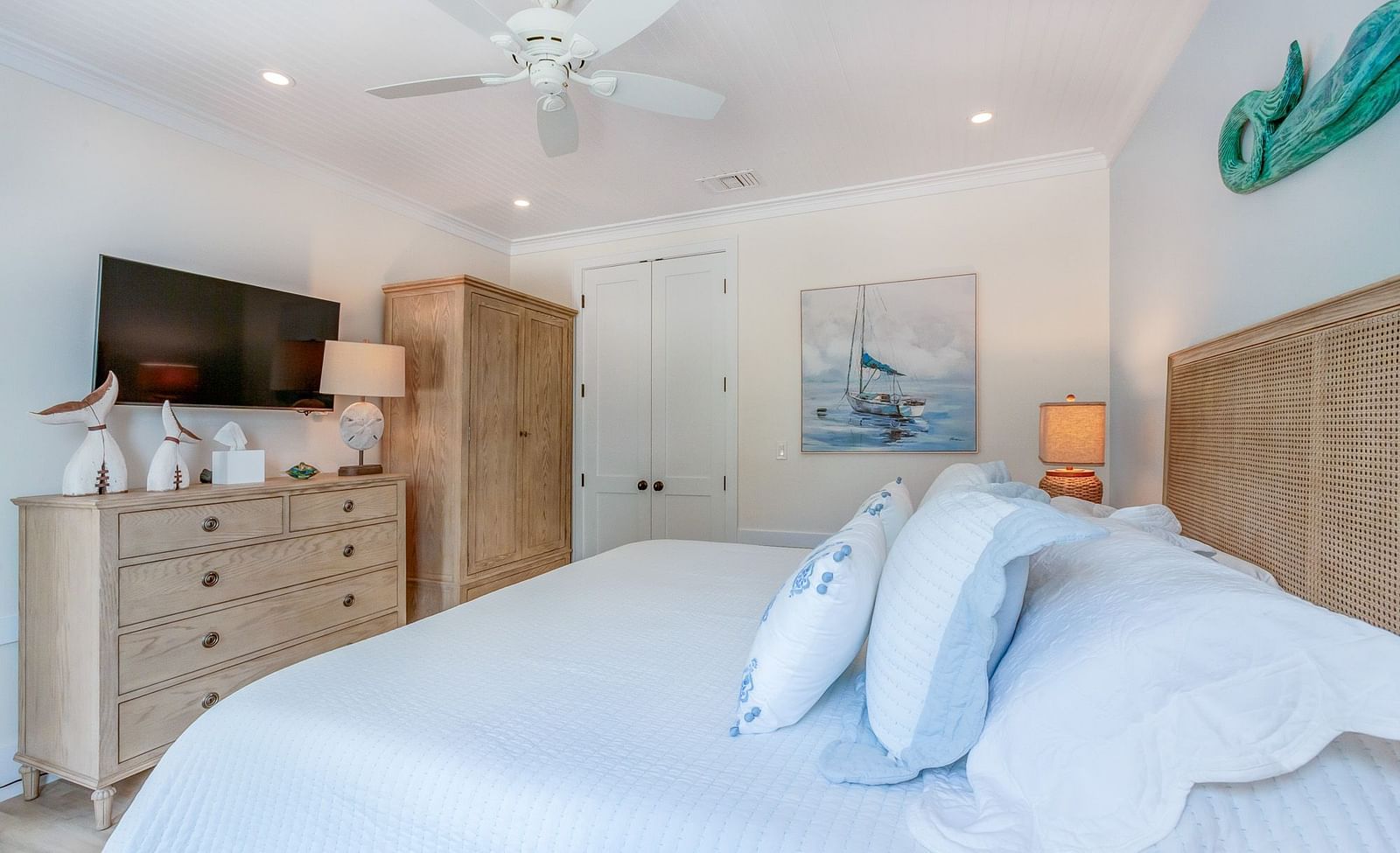 A bedroom with a huge bed with blue comforter, cupboards, TV, and wall arts at Abaco Inn.