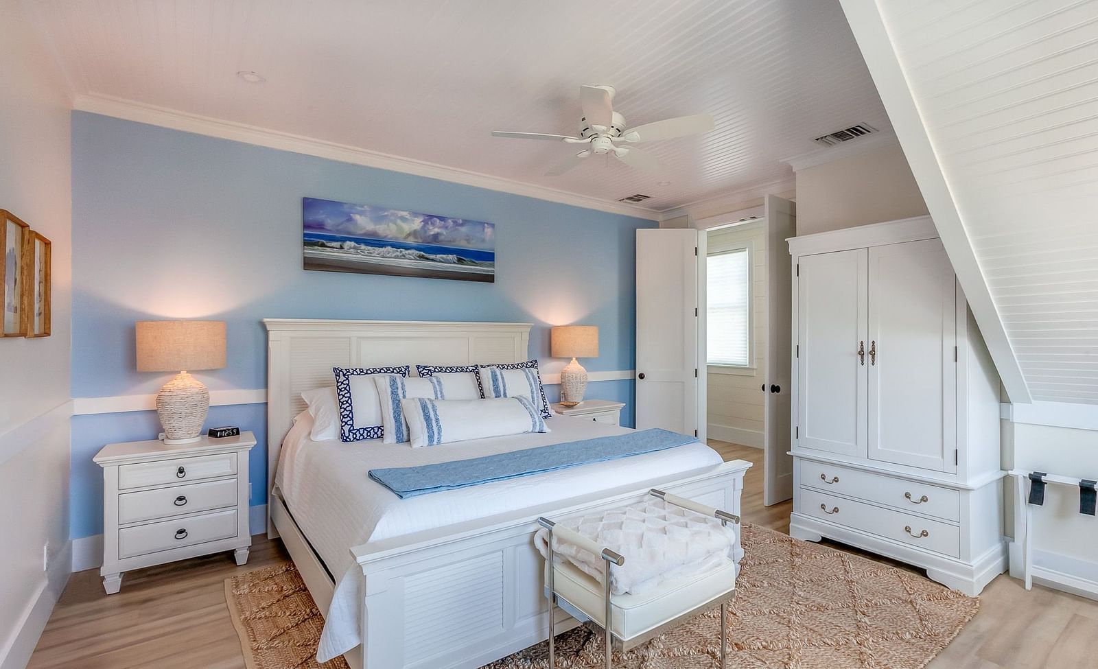a bright, blue and white themed bedroom with a huge bed, bedside drawer, wardrobe, wall decors and a door at Abaco Inn.