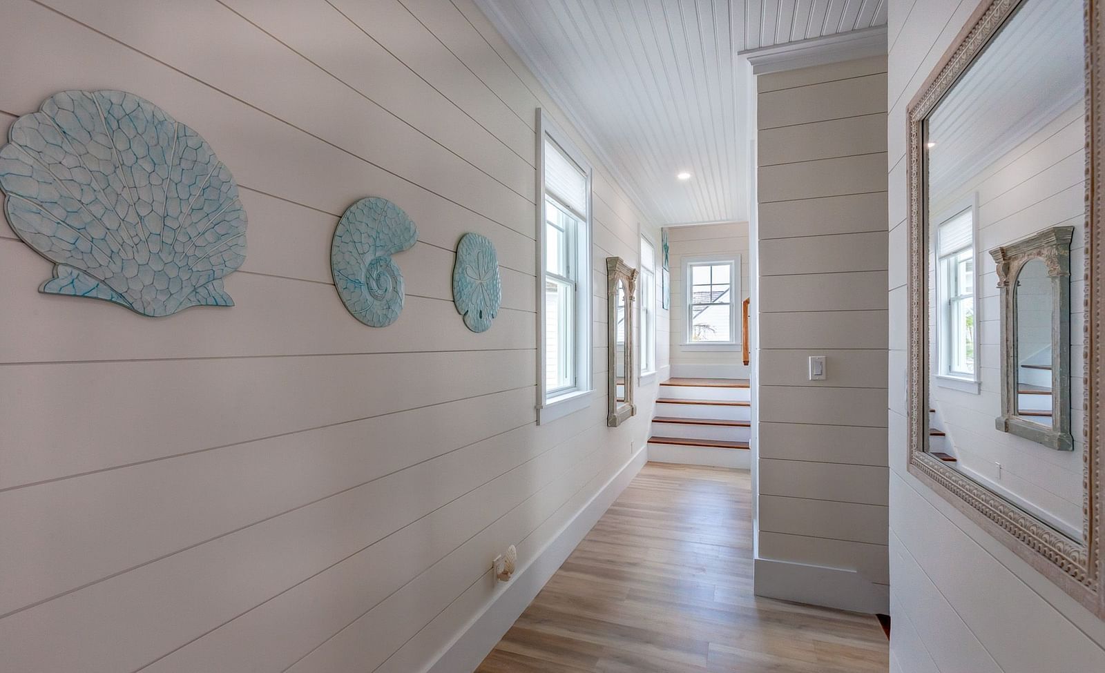corridor at Abaco Inn with wooden floor and white walls with mirror, seashell decors  and windows.
