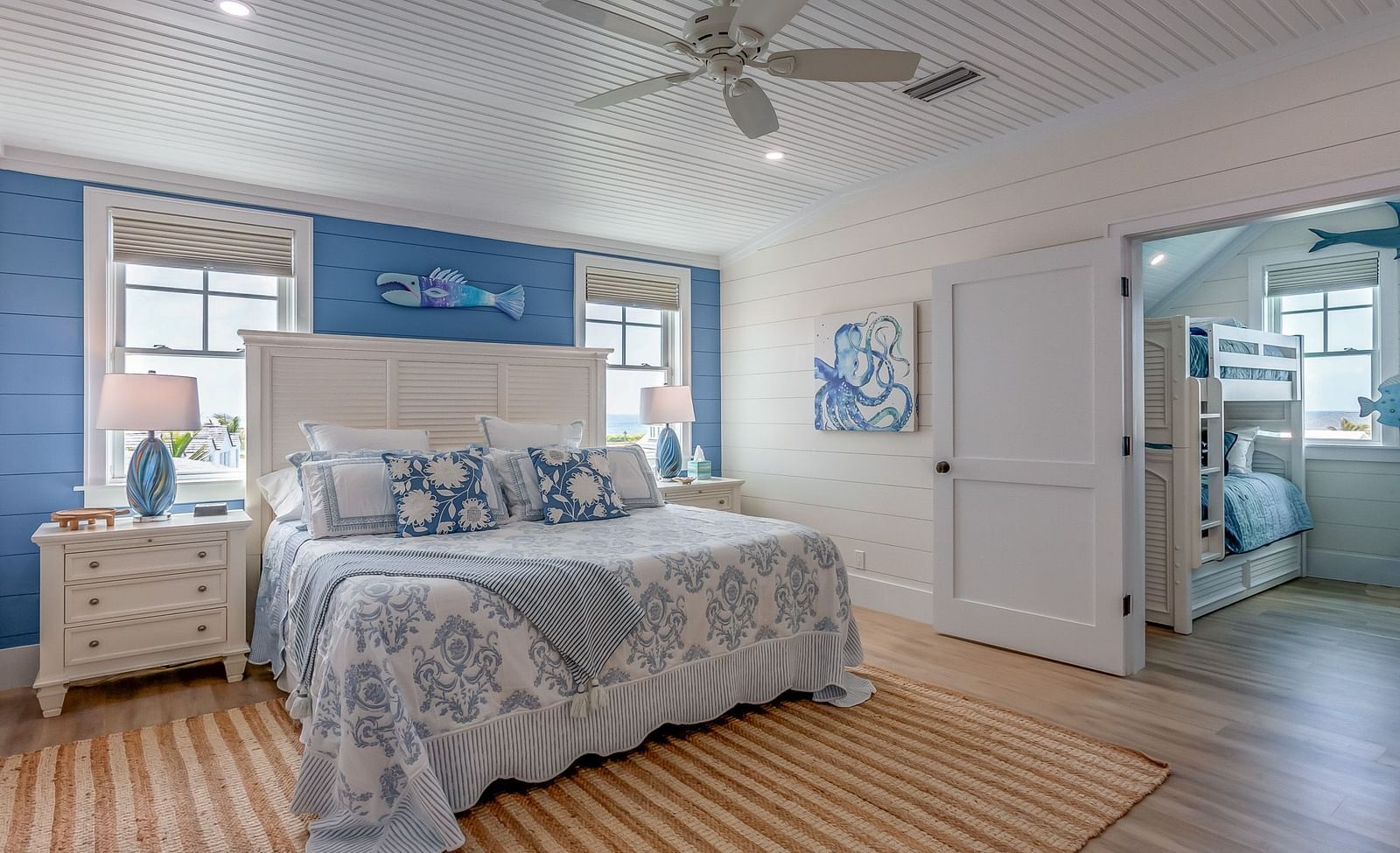 a blue and white themed, spacious bedroom with a huge bed, bedside drawers, wall arts, ceiling fan, windows, and a door that leads to a room with bunk bedsat Abaco Inn. 