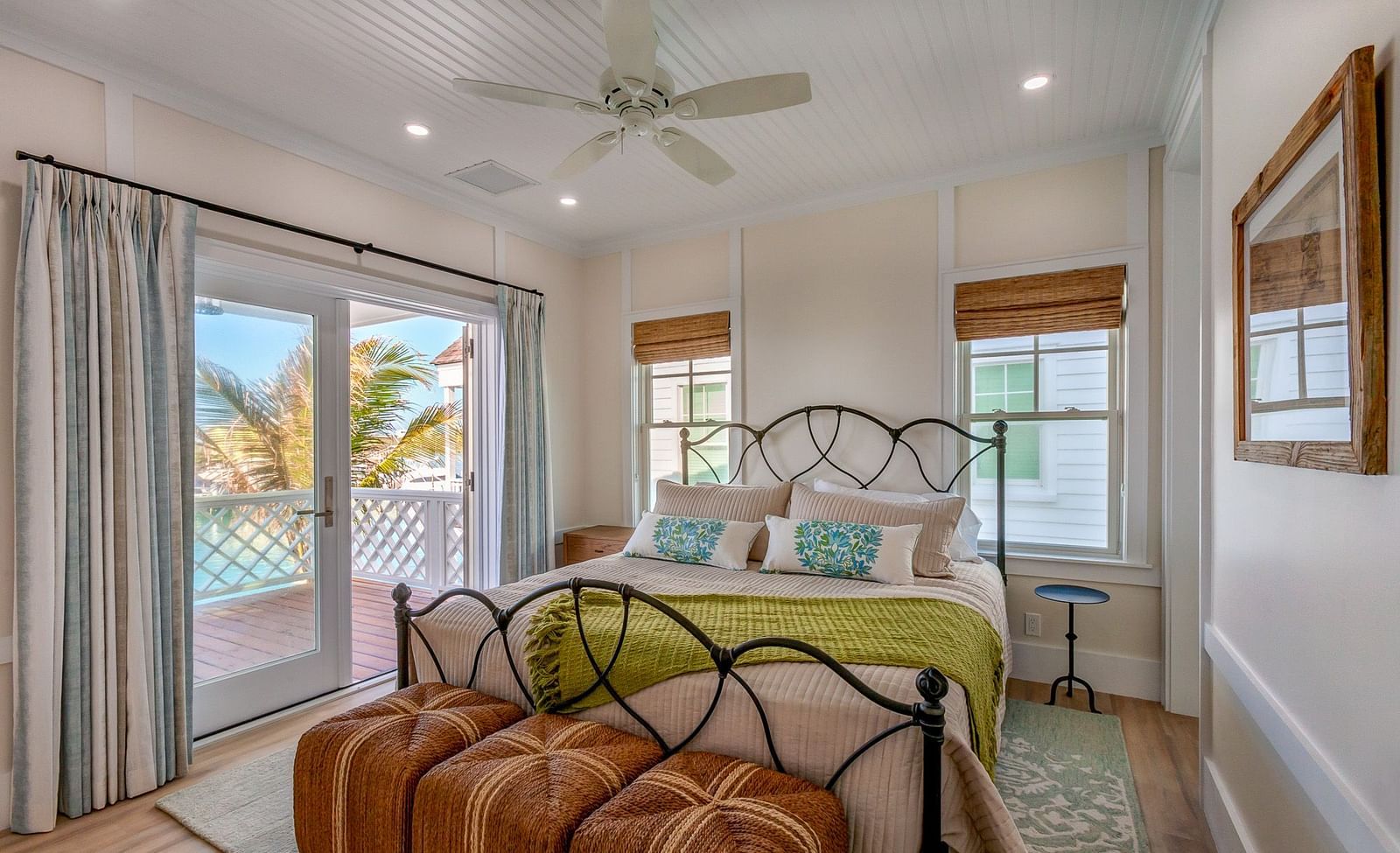 Well lit spacious bedroom with a huge bed on a decorative rug, ceiling fan, windows and a sliding glass door leading to the balcony with a sea view at Abaco Inn.