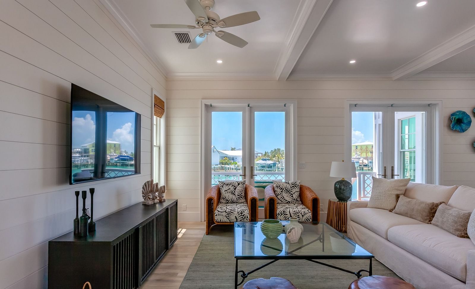 a sitting area with sofas , TV, a glass table, wall decors and windows overlooking greenery at Abaco Inn.
