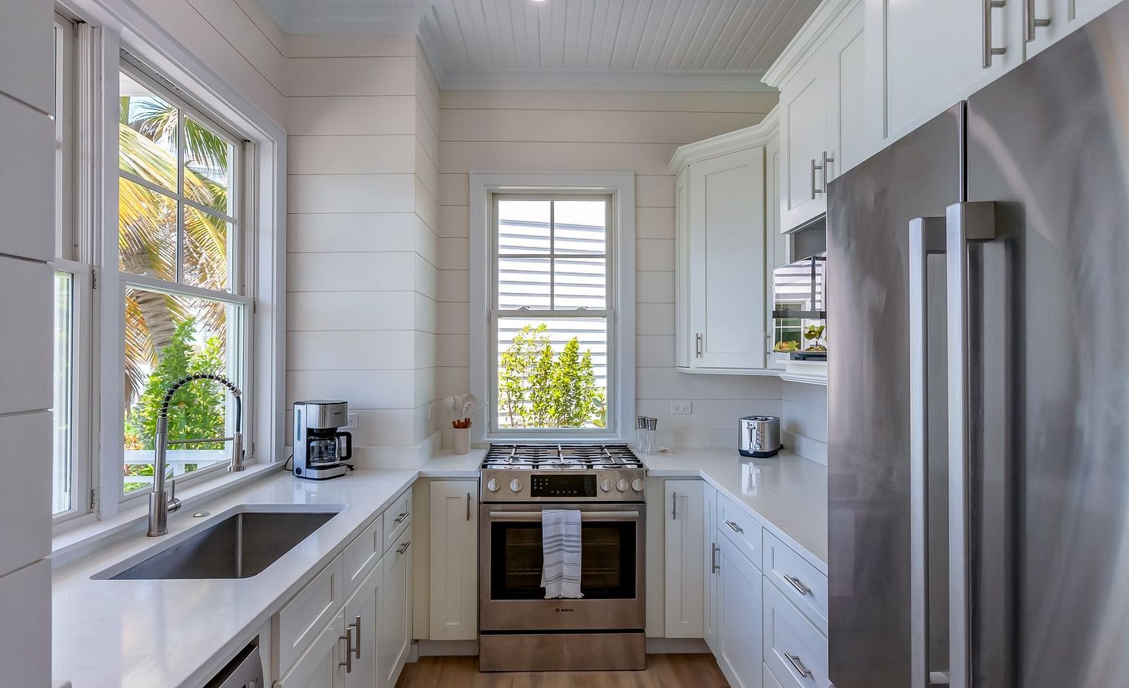 Bright and airy kitchen with a sink, oven, chimney, cupboards and windows overlooking greenery at Abaco Inn.