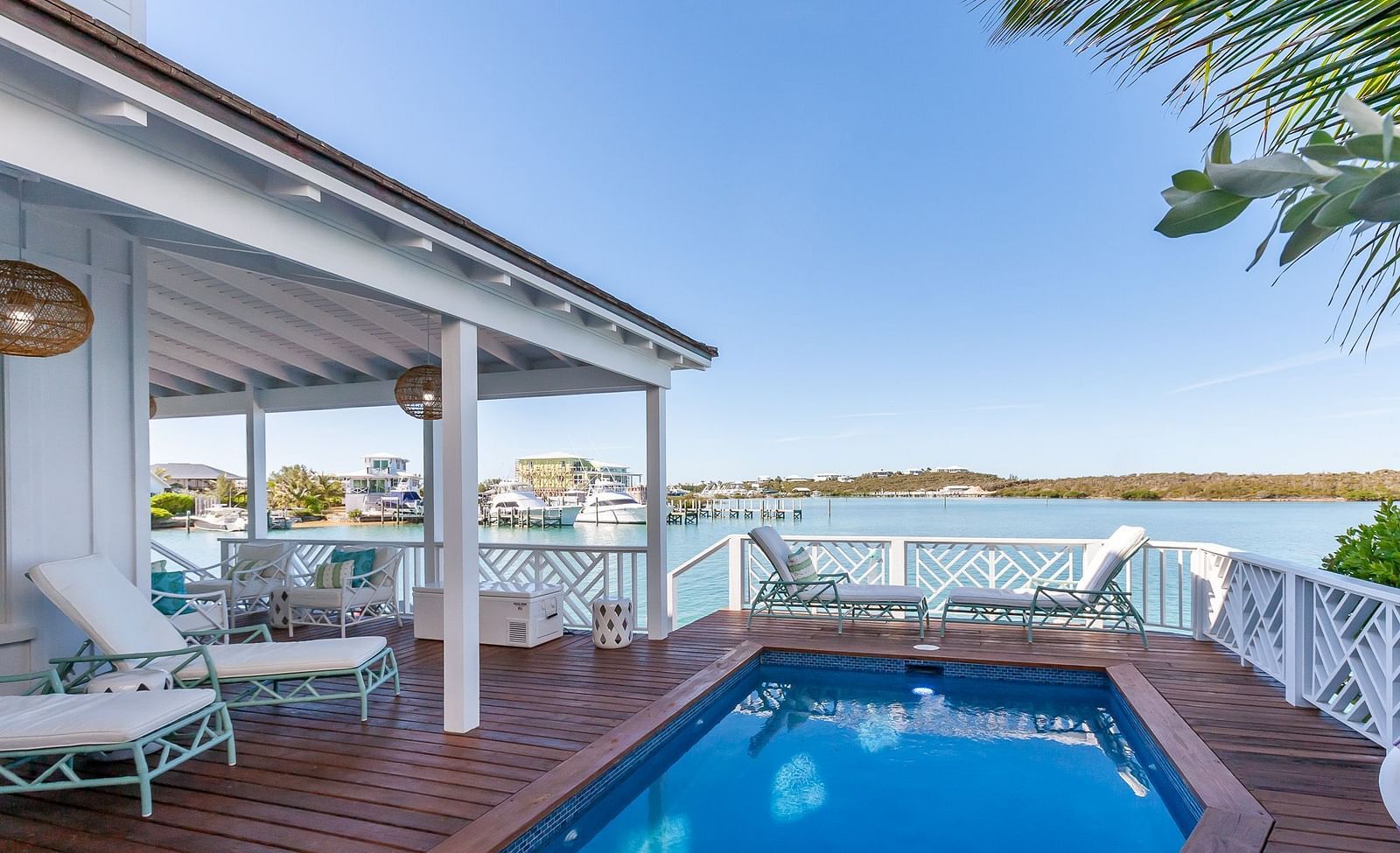 Private poolside deck with sun loungers and seating, overlooking a coastal bay with docked boats and distant hills at Abaco Inn