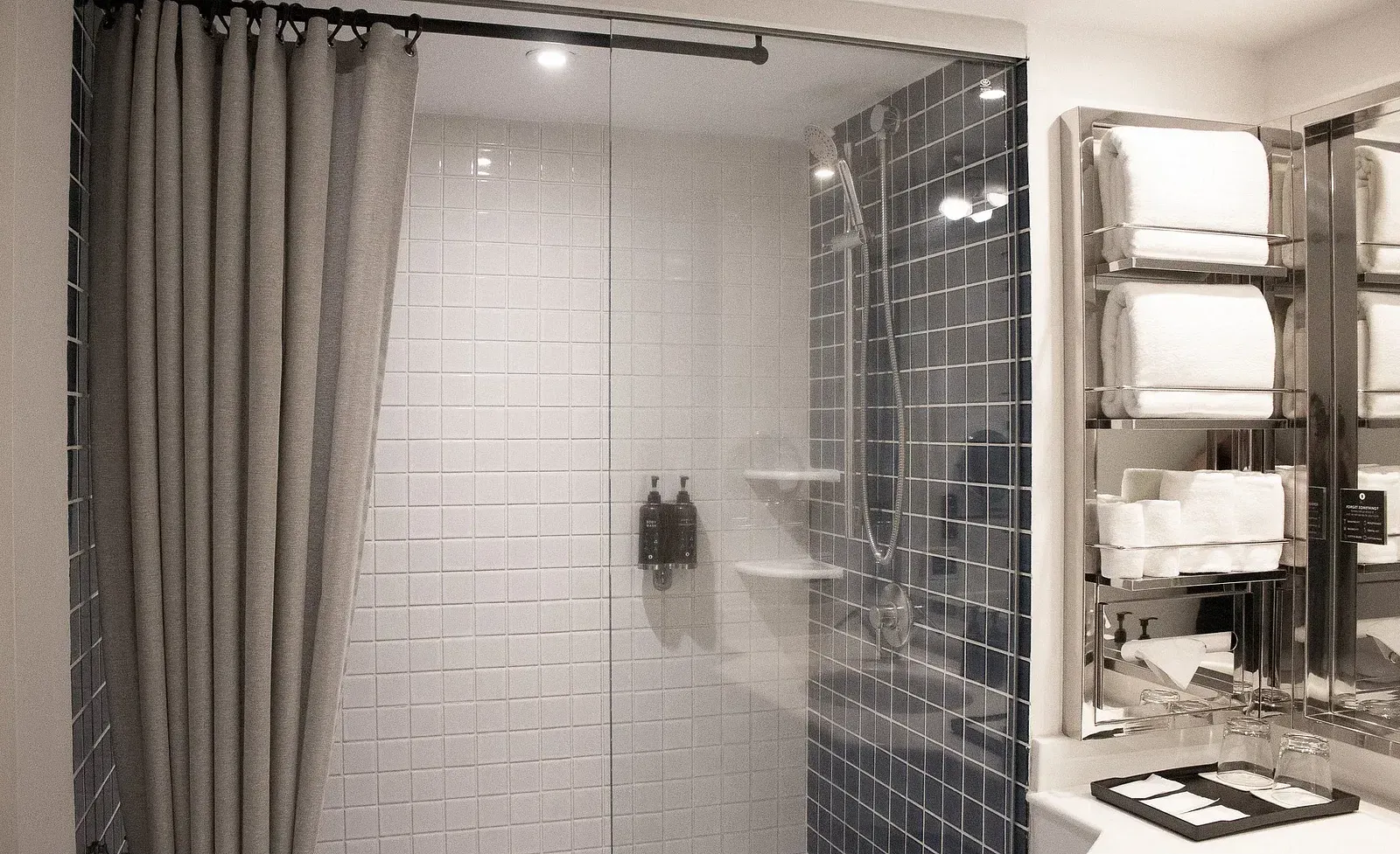 Contemporary hotel bathroom with dual-tone tiling, walk-in shower, grey curtain, white vanity, and modern fixtures in sleek monochrome design at Night Hotel Bangkok.