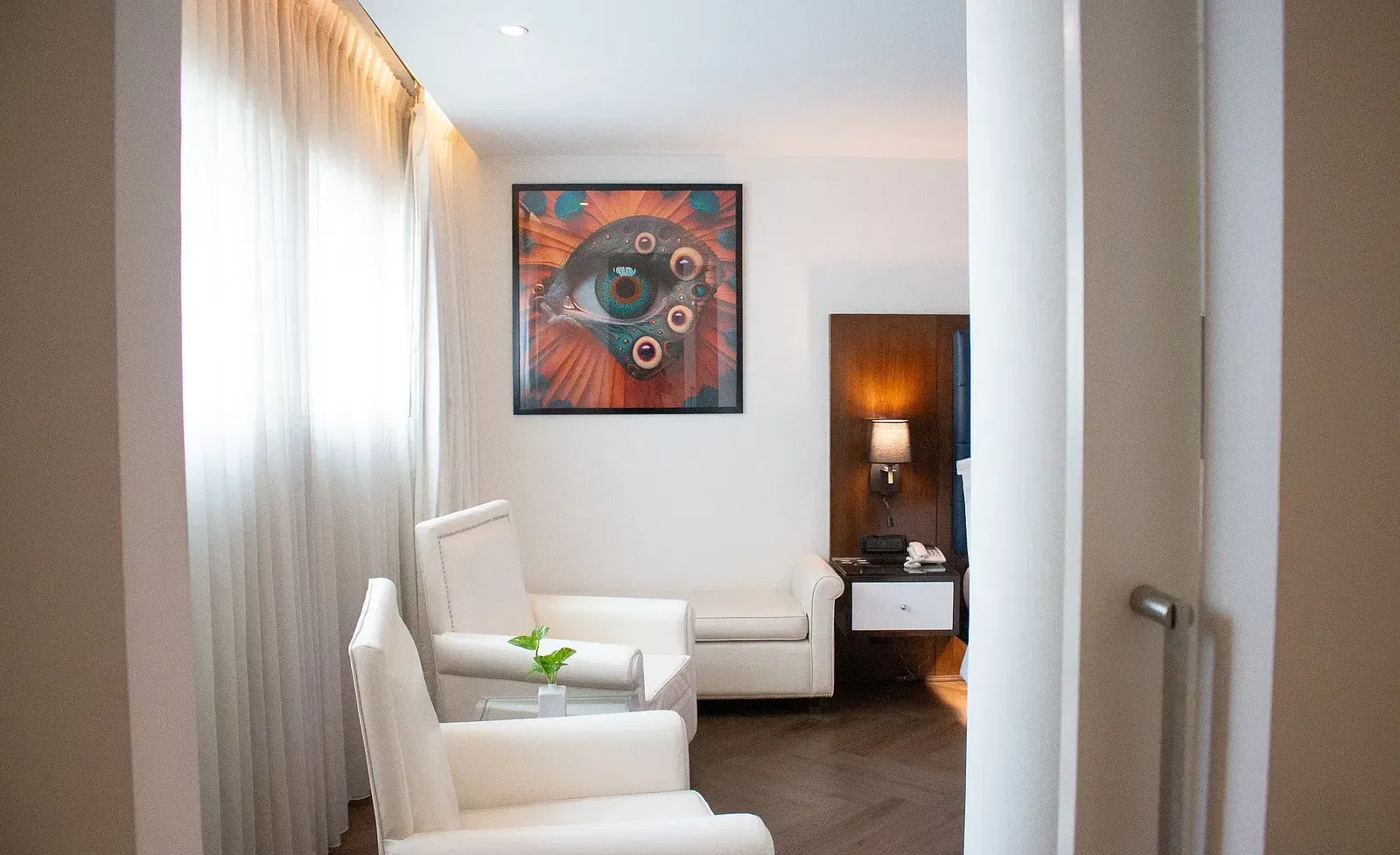 Stylish hotel seating nook with cream armchairs, colourful abstract artwork, walnut side table, and floor-to-ceiling windows with natural light at Night Hotel Bangkok.