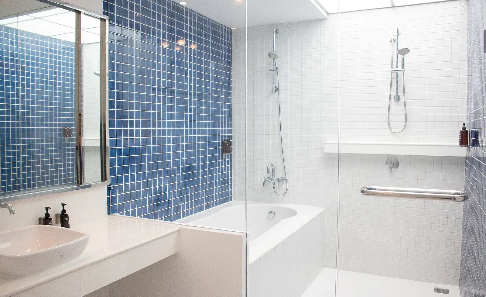 Spacious hotel bathroom featuring blue mosaic tiles, white subway tiles, modern bathtub, rainfall shower, and clean contemporary design aesthetic at Night Hotel Bangkok.