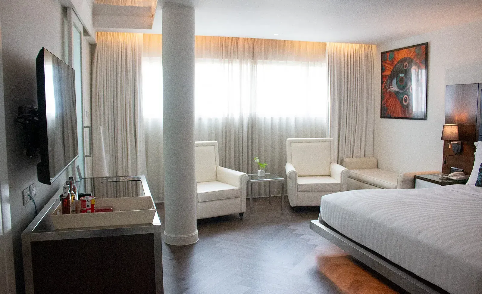 Premium hotel suite with structural column, cream seating area, entertainment console, large windows, and sophisticated neutral colour palette throughout at Night Hotel Bangkok.