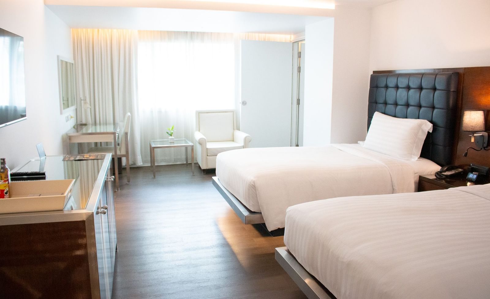 Spacious room with twin beds, wooden floor and curtained window at Night Hotel Bangkok.