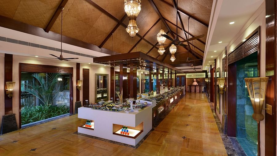 An overview of Oasis Restaurant with delicious delicacies on table and chandeliers on the roof - The Ananta Udaipur