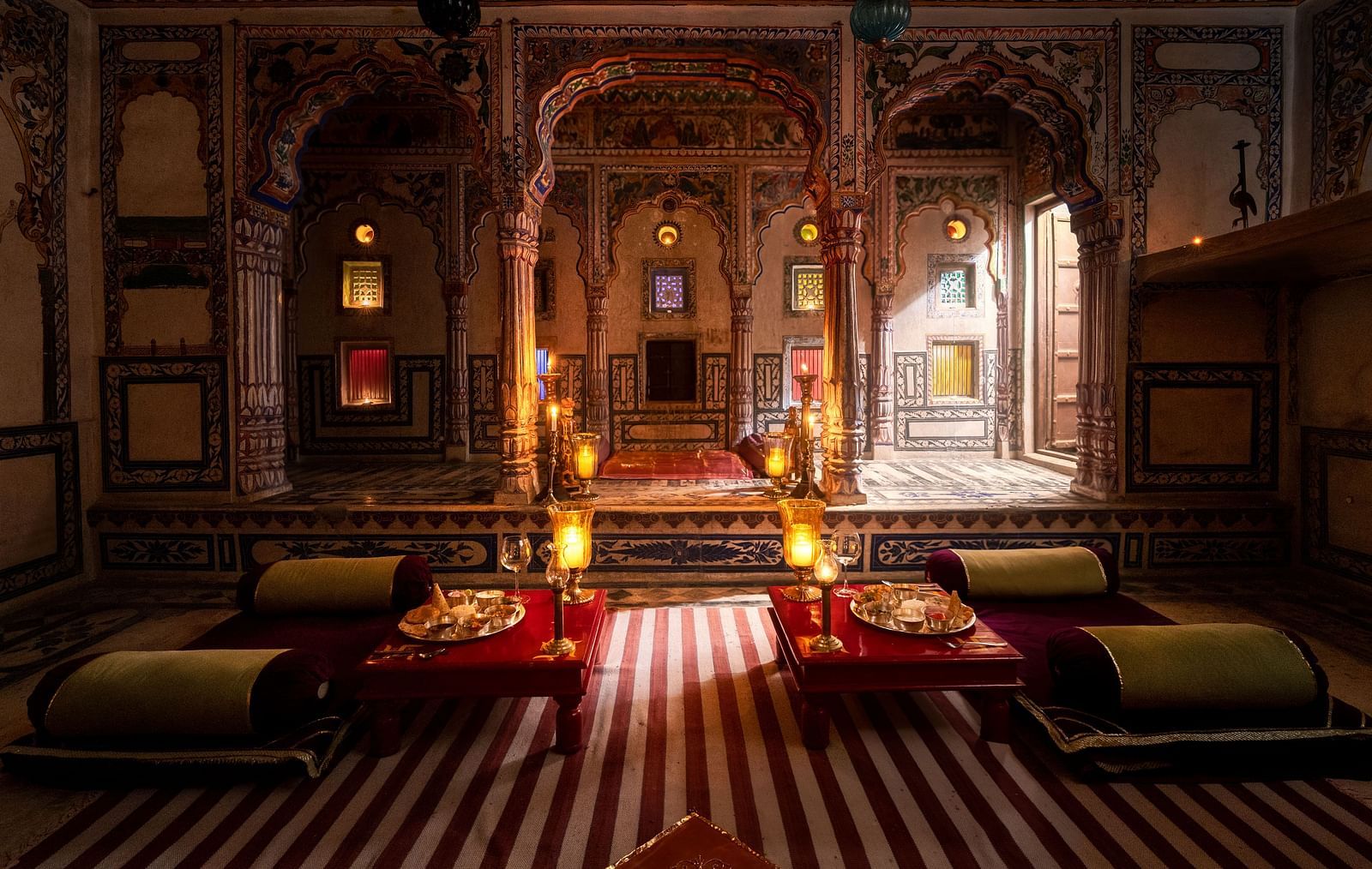 A richly decorated lounge at Fort Barli, featuring ornate arches, warm lighting, and plush seating, exudes a sense of historical grandeur and intimate ambience.
