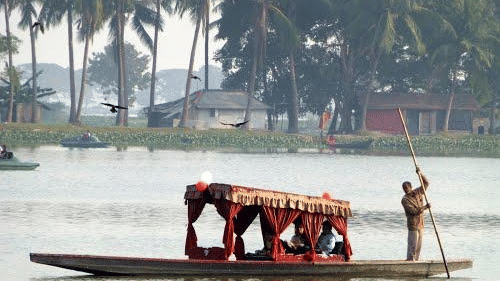 A boatman manoeuvres a traditional long boat with brightly-coloured curtains across the calm waters of Nalban, Kolkata.
