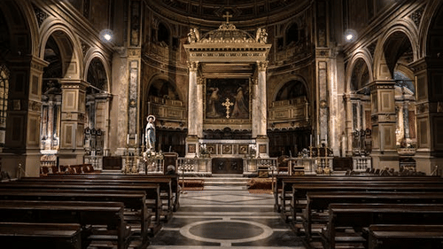 interior view of a cathedral with benches and altar in view and lights on the wall