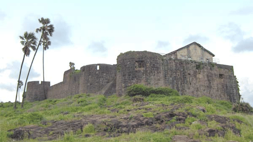 A stone fort wall with round bastions on a hill with a coconut trees beside it.