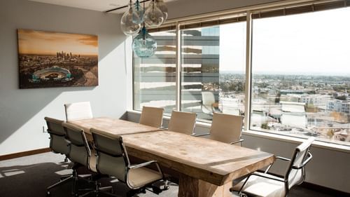 Image of a boardroom featuring chairs placed around a large rectangular table with the view of the city in the background from the window