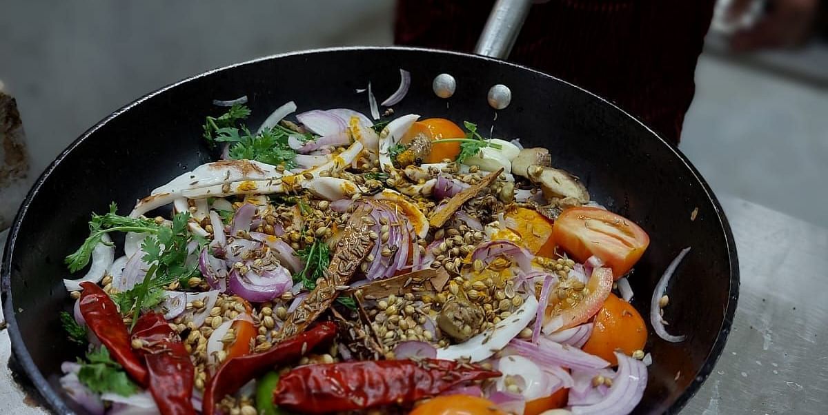 A colourful pan of fresh ingredients including onions, tomatoes, garlic, spices, and herbs being prepared near Matsya Island Retreat 