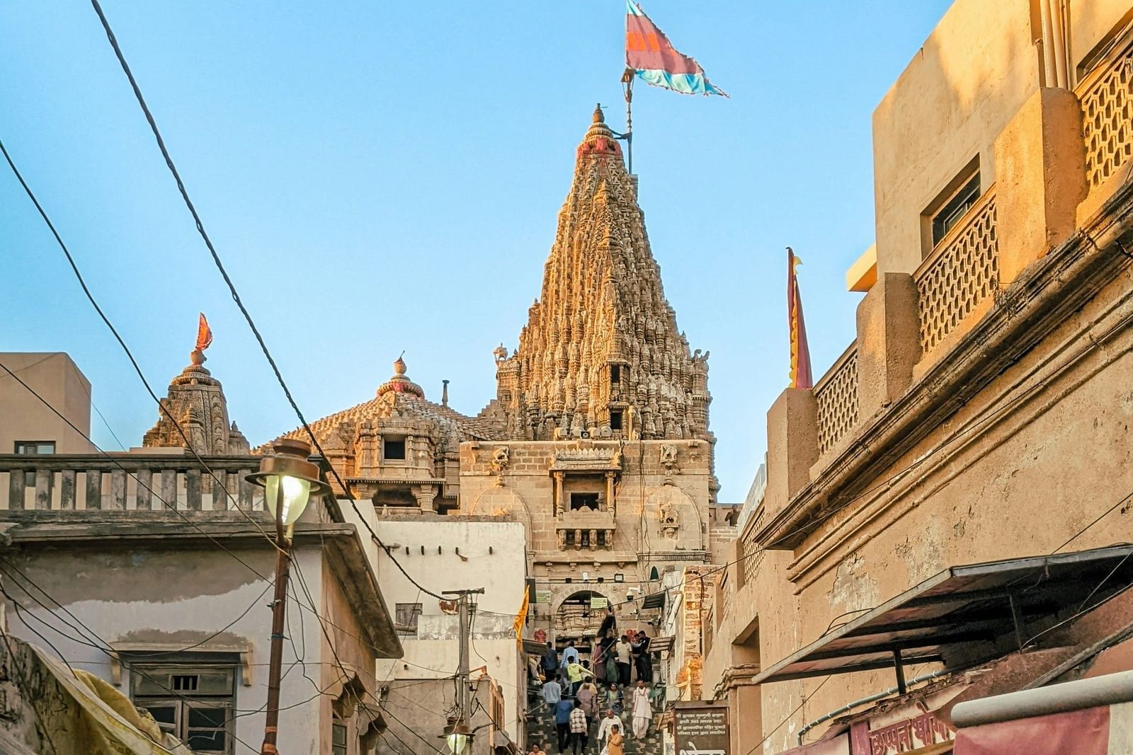 A crowded street leading up to an ornate temple with a flag flying from its peak.