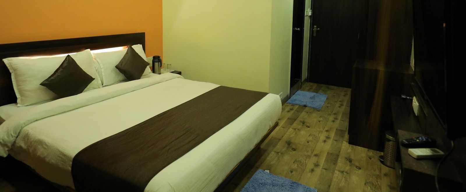 Executive Room with wooden flooring in Krushnai Resort, featuring a king size bed with brown runner, air-conditioner and a wardrobe.