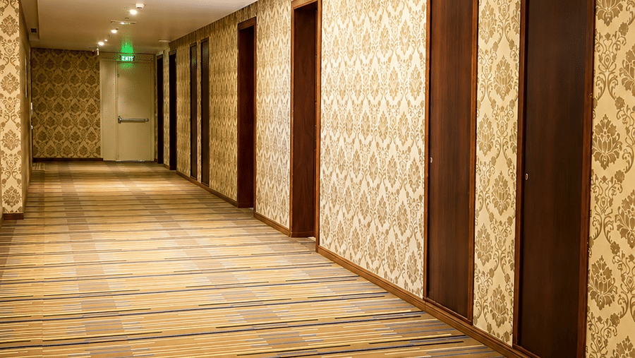Narrow hotel corridor at Golden Tulip Kukas Jaipur with striped carpet flooring, warm recessed lighting, and clean beige walls.
