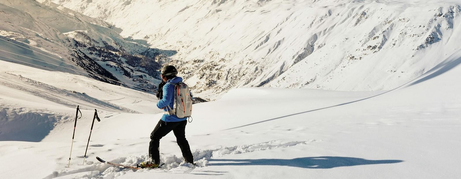 Picture of  a person skiing down a snowy slope, with snowy mountains in the background.
