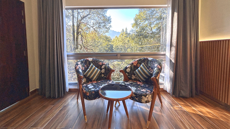 A close up shot of two chairs and a coffee table with a large window through which sunlight is beaming into the room - DLS The Emerald, Nainital