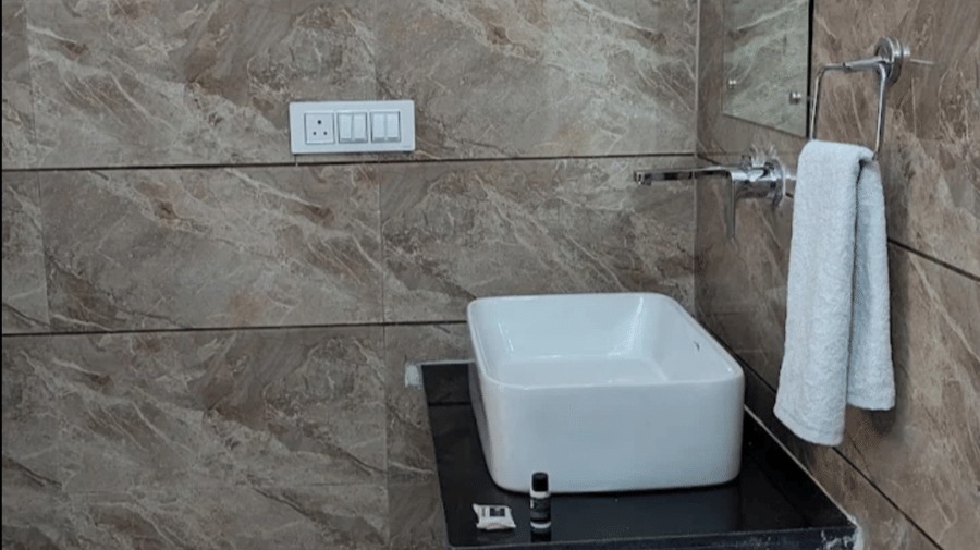 A modern bathroom interior at Estherea Bagh, Ranthambore, showing a sink on a counter against textured wall tiles.