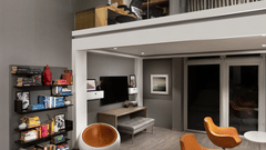 A spacious, modern multi-level living area at The Atara, Gurugram features an upper mezzanine level, a large bookshelf, a comfortable sofa, and a stylish armchair, creating an open design