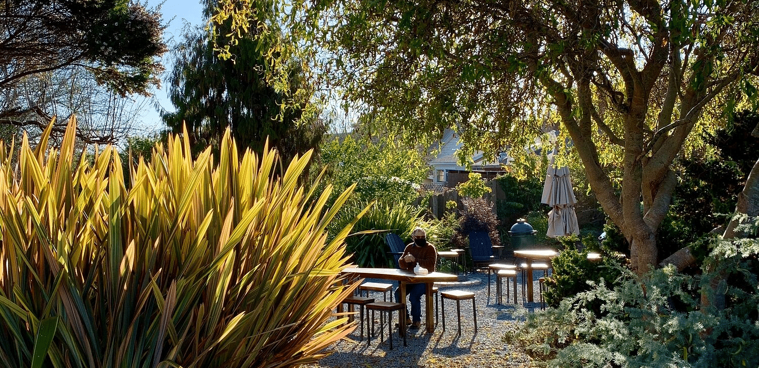 A sunny garden path leads to an outdoor seating area with tables and chairs.