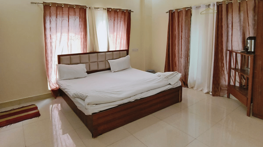 A hotel room in Bhopal featuring a double bed with white bedding, dark wood flooring, an air-conditioner, and a large window | Nandan Resort