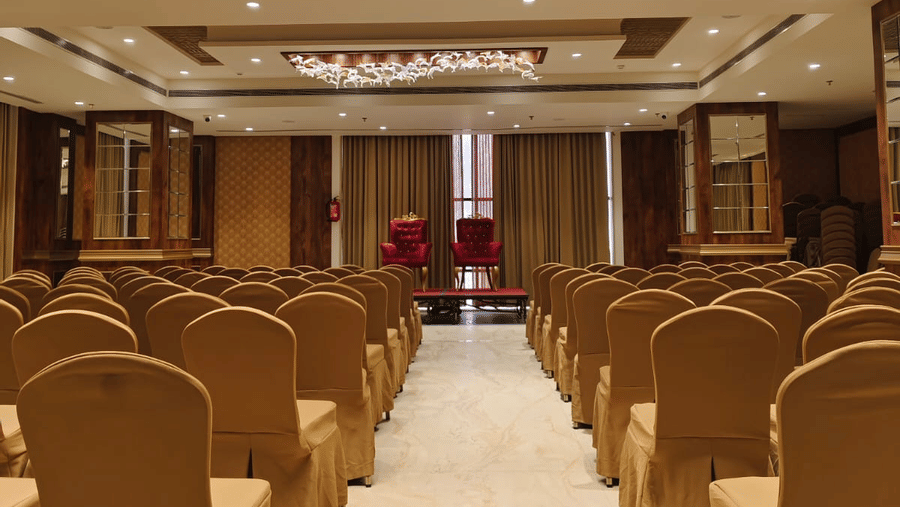The Raj Darbar banquet hall showing rows of gold-covered chairs and a white carpeted aisle leading to the stage area - Skkylight Lords Inn, Nanded