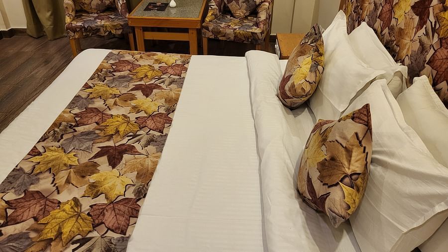A close-up of a bed with floral-themed cushions and a seating arrangement at Dagshai Manor Kasauli - Inde Hotels.