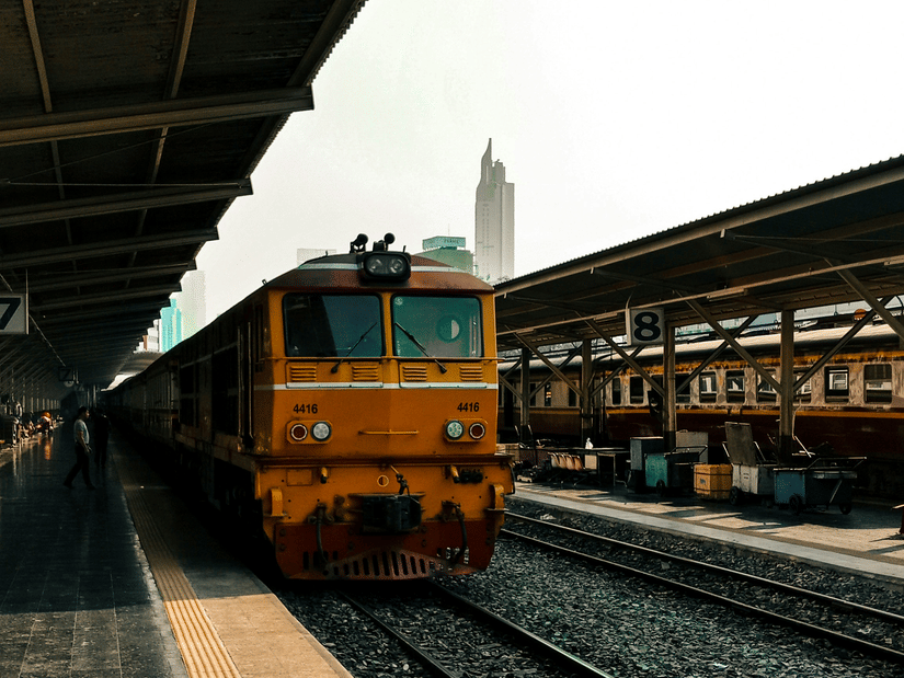 A train at the railway platform with passengers waiting nearby, tracks stretching ahead, and station roof covering part of scene