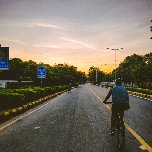 A cyclist rides along a quiet road as the sun sets over the surrounding landscape.