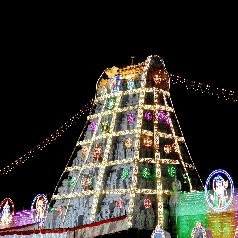 A view from a distance of a temple in Tirupati, with lights over the gopuram during a celebration.