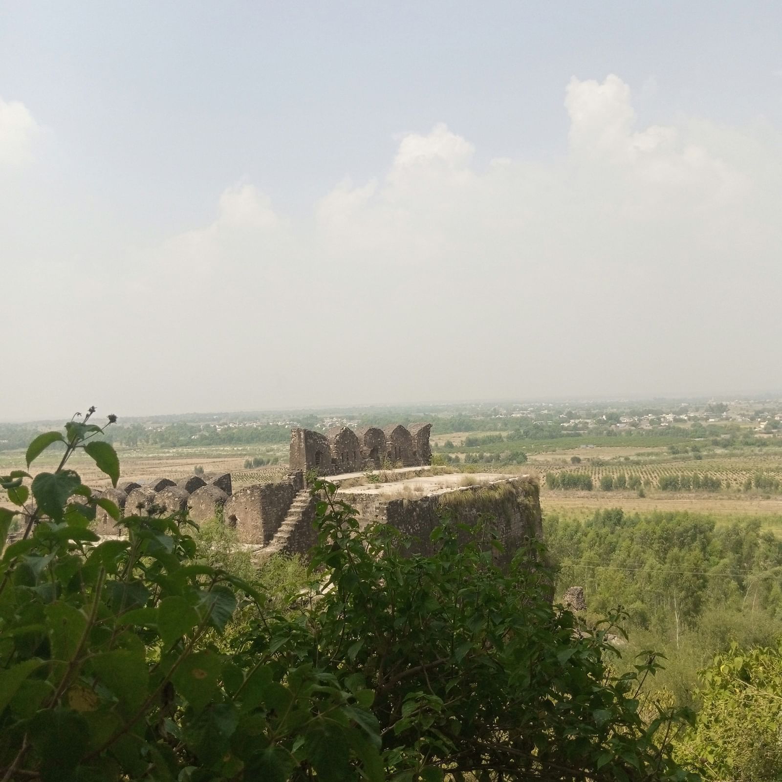 A scenic view of a fort atop green hills, surrounded by misty landscapes under a pale sky.