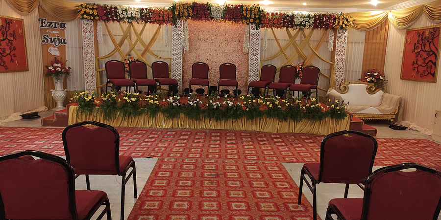 Indoor wedding or event setup with red chairs arranged in rows, facing a flower-adorned stage at the front - Black Thunder, Coimbatore