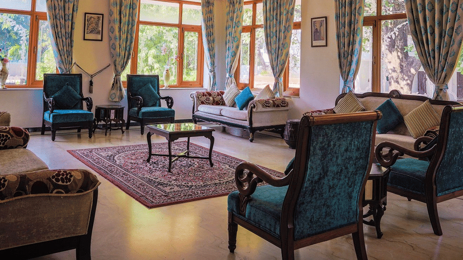 A lobby lounge area featuring armchairs, a sofa, a central rug, and multiple curtained windows at Amantra Shilpi Resort, Udaipur.